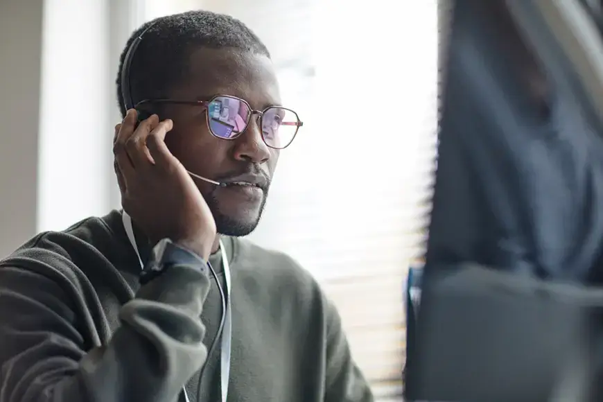 Portrait of Black young man speaking into headset with microphone while consulting client on IT customer support line copy space